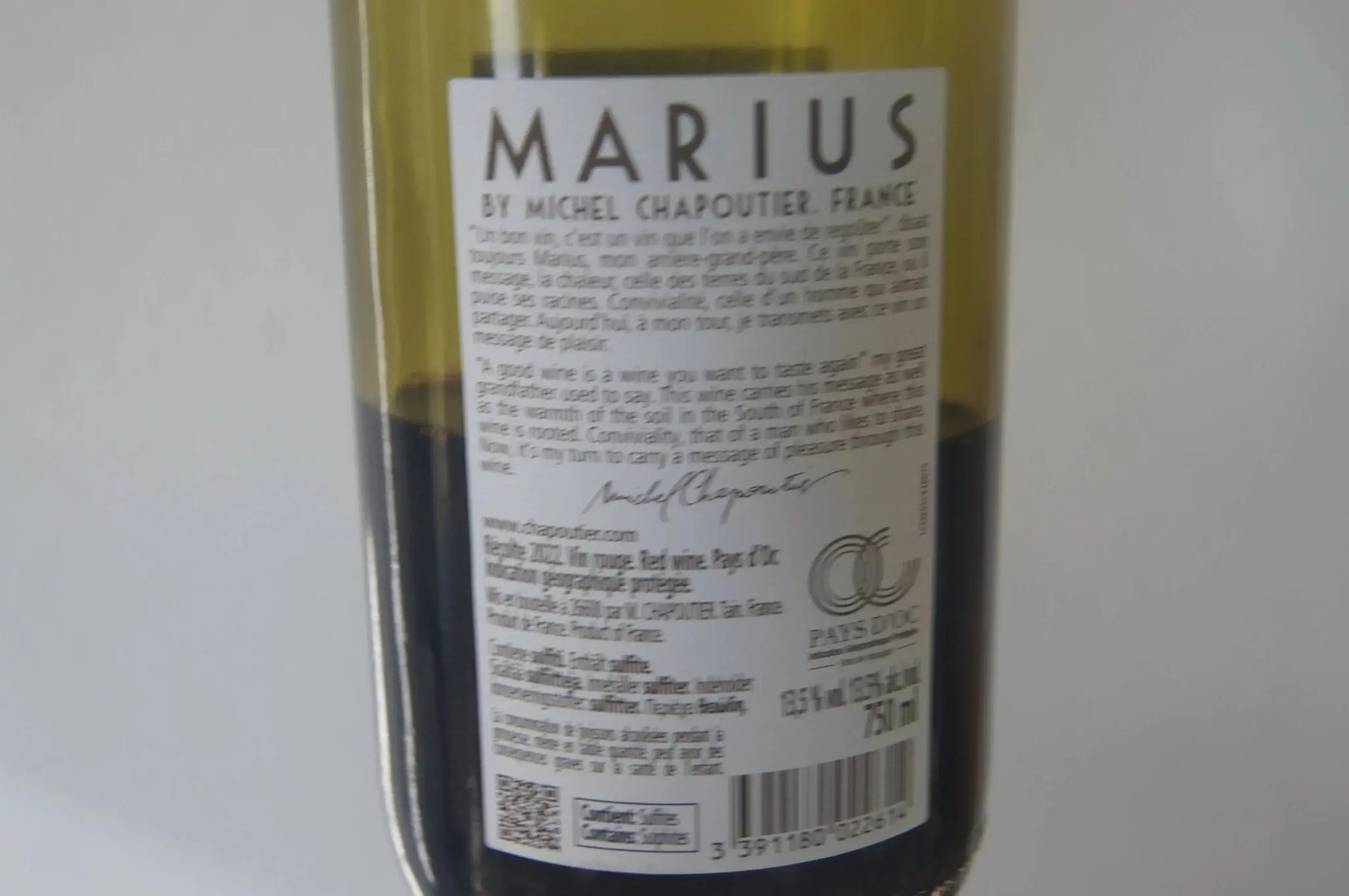 Flasche des Marius 2022 Rotwein aus Südfrankreich, platziert auf einem Holztisch neben einer Auswahl von Speisen, die seine Vielseitigkeit in der Paarung mit verschiedenen Gerichten unterstreichen."